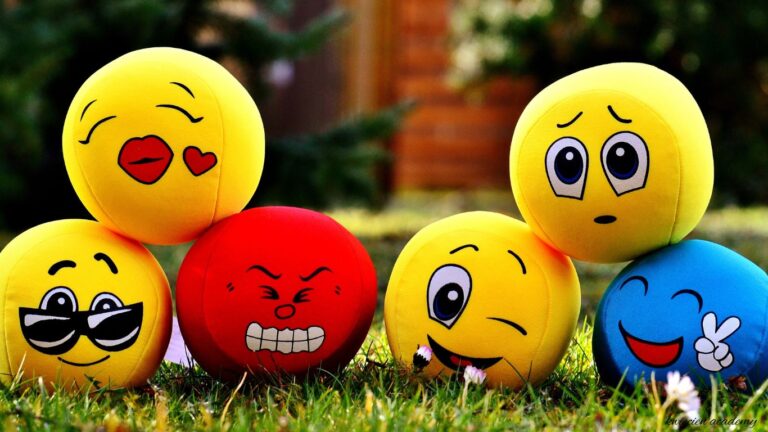 Kolorowe piłeczki z emotikonami emocji leżące na trawie