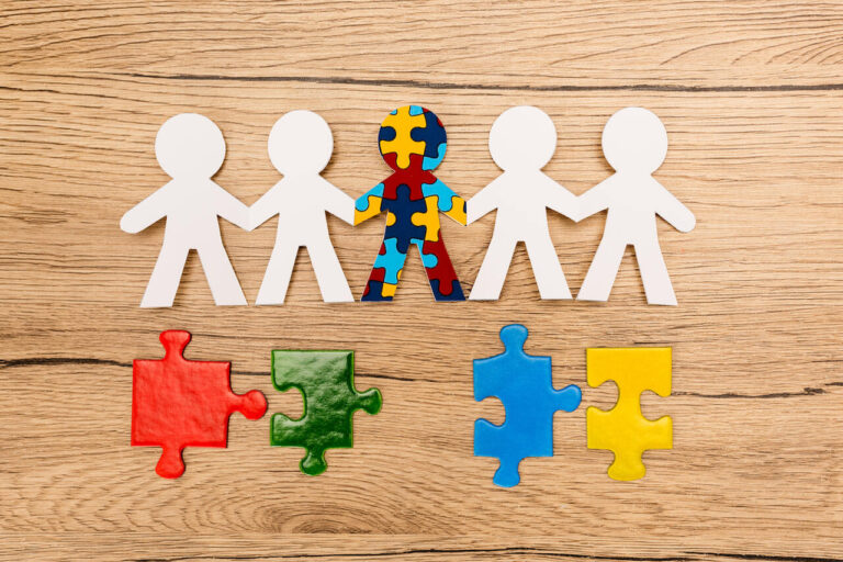 Papierowe sylwetki ludzi i kolorowe puzzle na drewnianym tle — symbol autyzmu